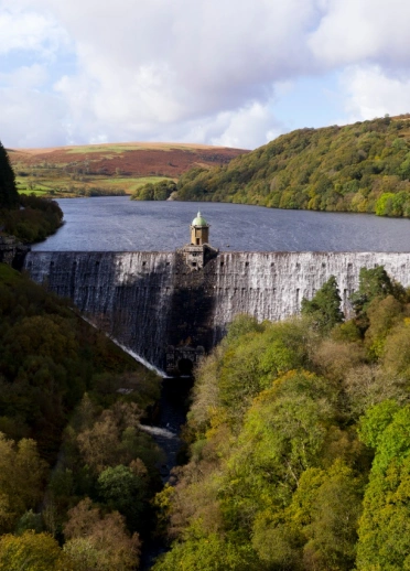 A dam holding back the river framed in trees turning colour in the autumn.