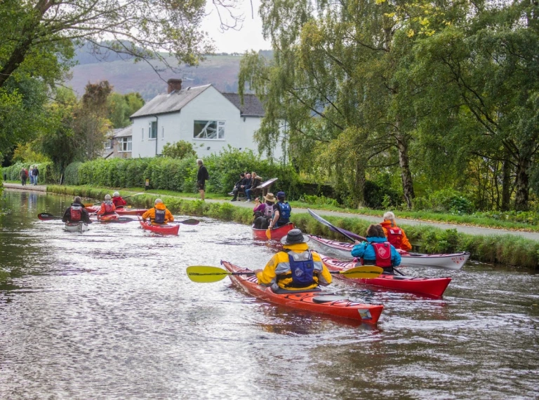 A group of people canoeing down a river in colourful protective waterproofs.