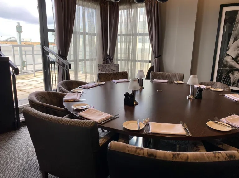 A round dining table in a private room with large windows leading onto a rooftop balcony.