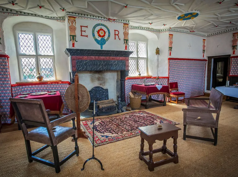 A room with an ornate fireplace, decor and wooden chairs in an historic house.