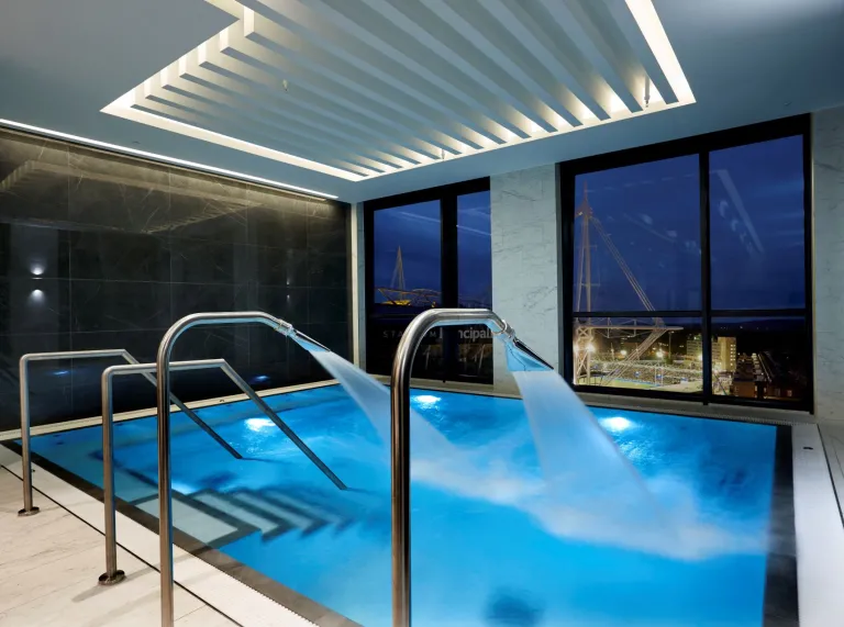 A spa pool with spraying fountains against large glass windows in a hotel.