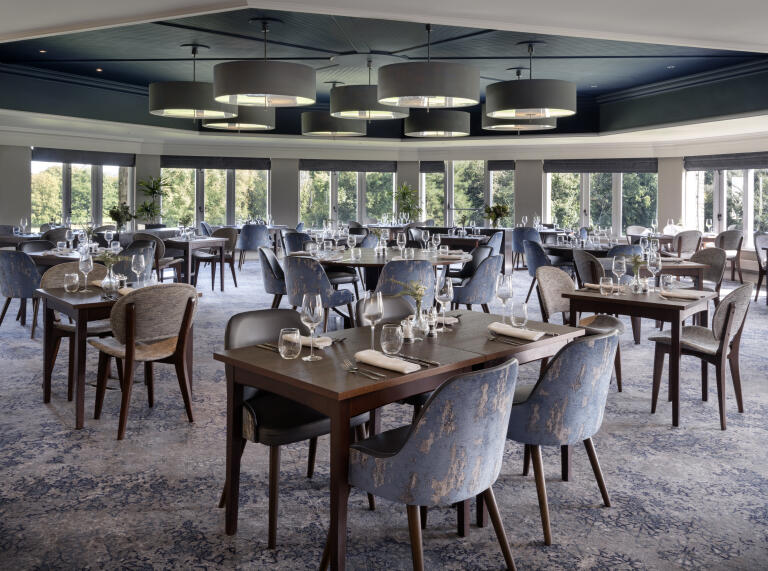 wooden tables and cushioned chairs set out overlooking green trees 