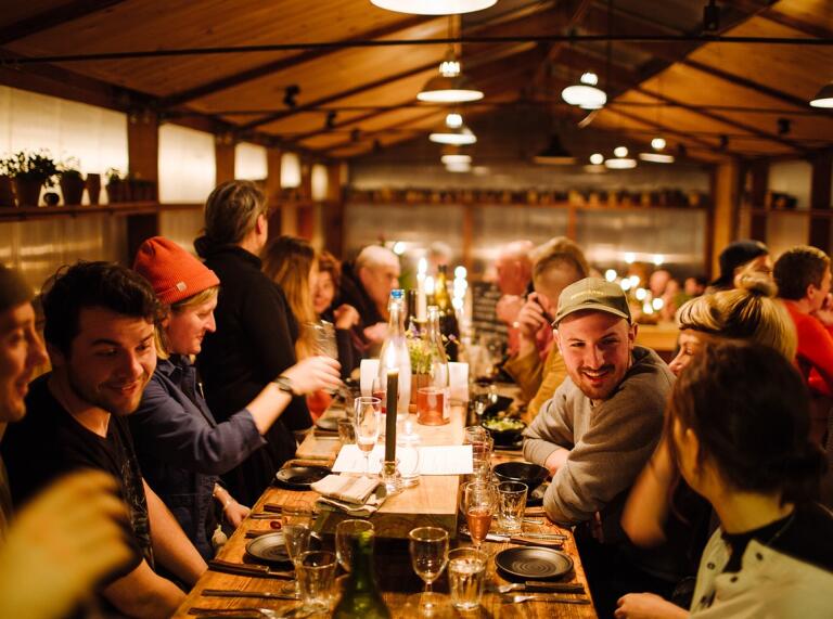 People dining in the farmhouse with low lighting and candles at a large dining table