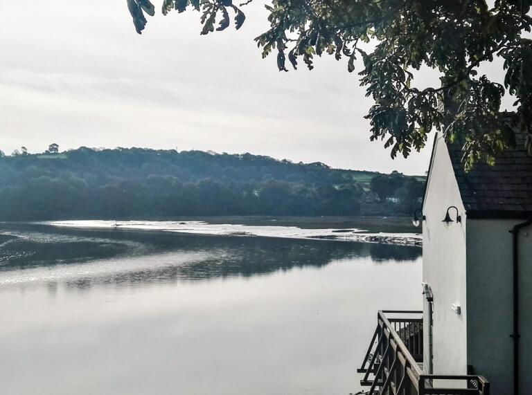 the boathouse building overlooking the estuary waters with trees in the background