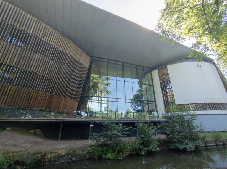 Outside of  building with blue water and trees against the glass foyer entrance 