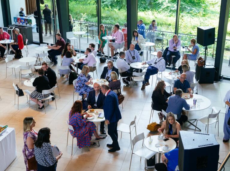 people standing in the foyer talking at the conference with green trees outside and sun shining