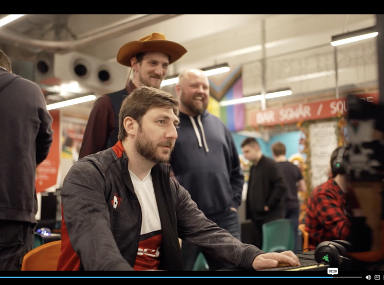 John Jackson sitting at the computer with two people standing behind laughing one wearing a cowboy hat 