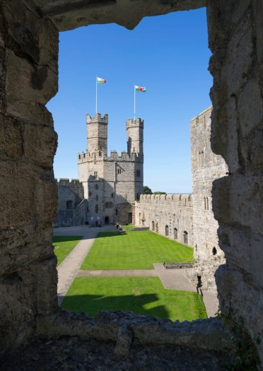 View through a castle window of the twin towers of a castle with welsh flags flying from them.