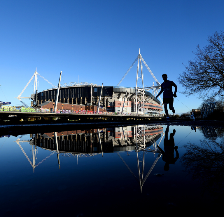 Principality Stadium which is reflected in the river with a jogger running by.