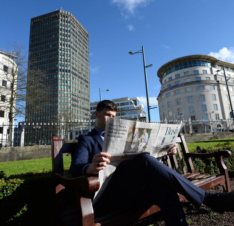 A gentleman reading the newspaper in a city centre.