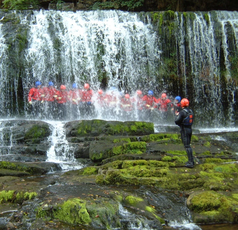 Group in safety gear standing behind a waterfall.