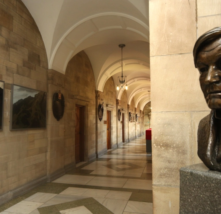 Aspects of Main Arts Building Bangor University with stone walls tiled cream floor and head statue of man in the forefront.