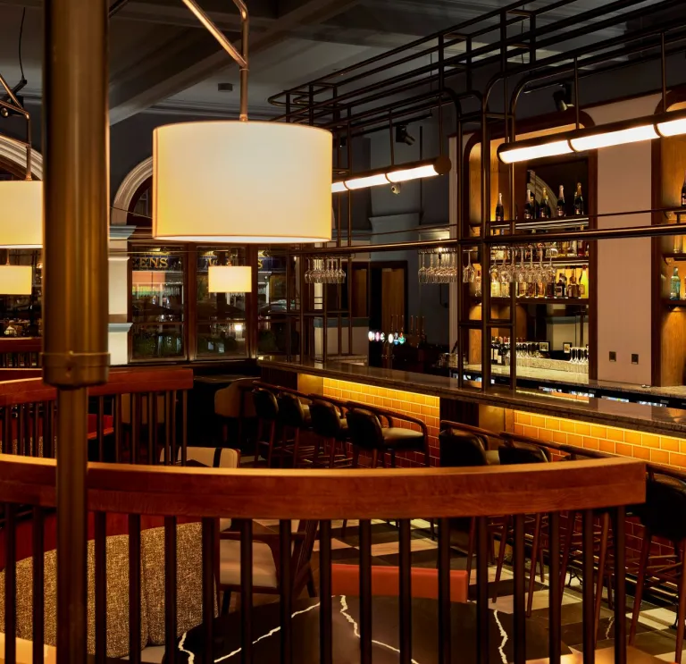 A restaurant in a hotel with bar stools against the fully stocked bar.