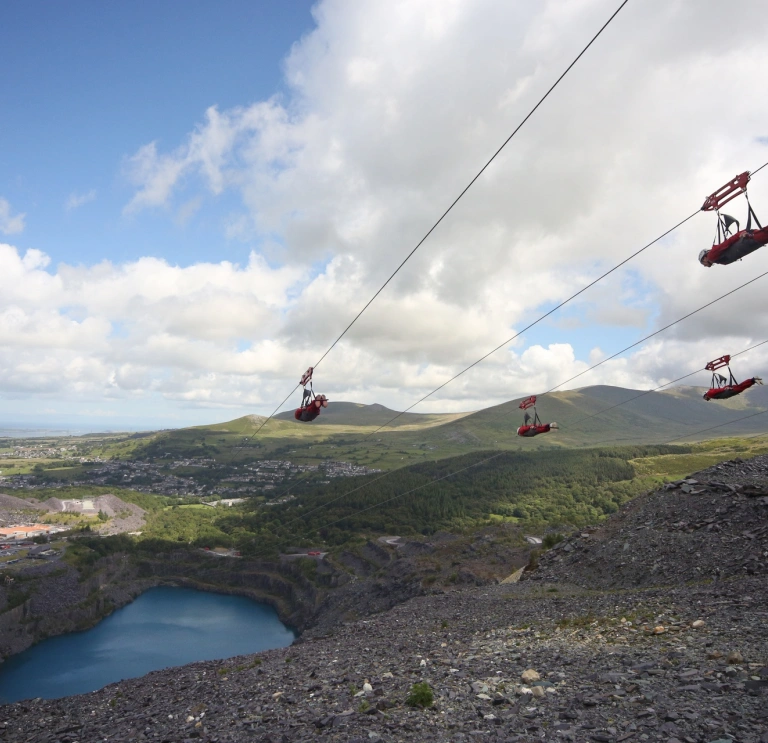 People zipping down a former quarry and the blue reservoir below