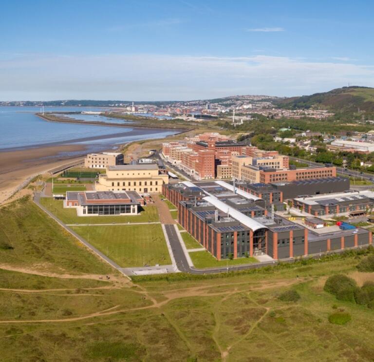 Swansea University exteriror aerial shot with building on the sand and blue sea behind 