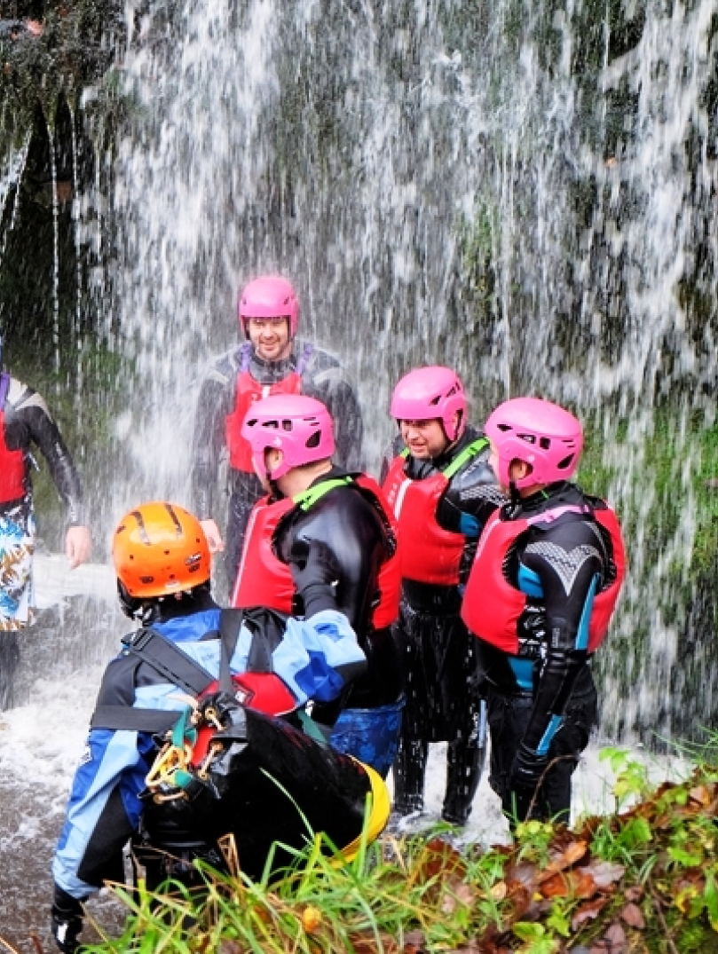 A group of people under a waterfall wearing safety gear.