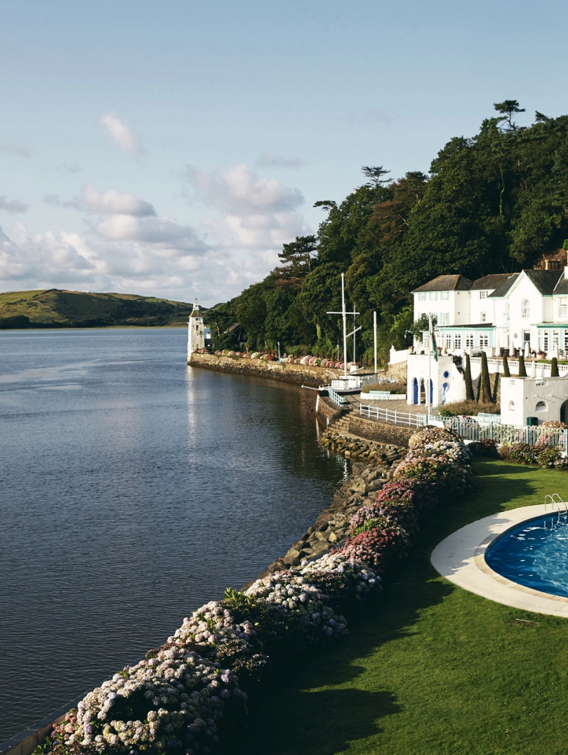 A white-fronted hotel and outdoor swimming pool by a river.