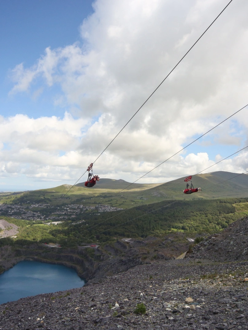 People zipping down a former quarry and the blue reservoir below