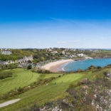 Views of golden sands and the ocean from a golf course up on a cliff.