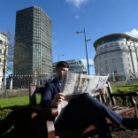 A gentleman reading the newspaper in a city centre.