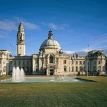 A city hall with a fountain on the lawns at the front of the building.