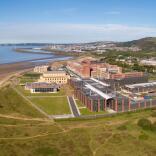 Swansea University exteriror aerial shot with building on the sand and blue sea behind 